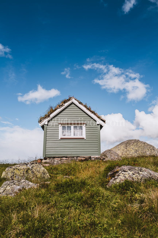 挪威风景秀丽的韦斯特兰 (Vestland) 上有一间古雅的小屋，屋顶呈绿色，背景为蓝天。