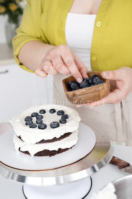 模糊女性糕点师装饰蓝莓奶油蛋糕