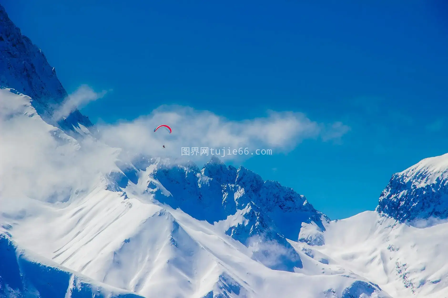 冬日蓝天雪山滑翔伞翱翔图片